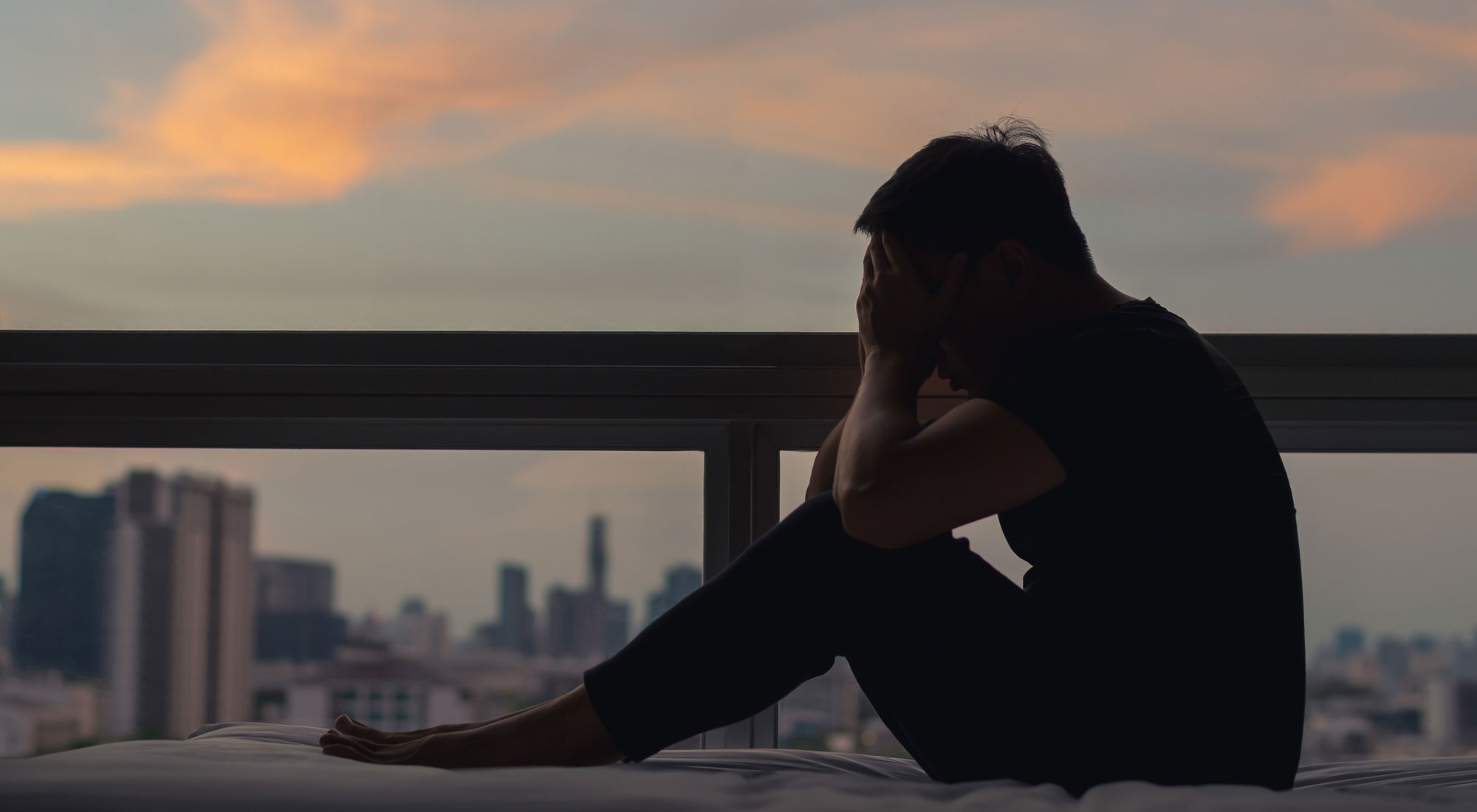 man sitting on bed depressed